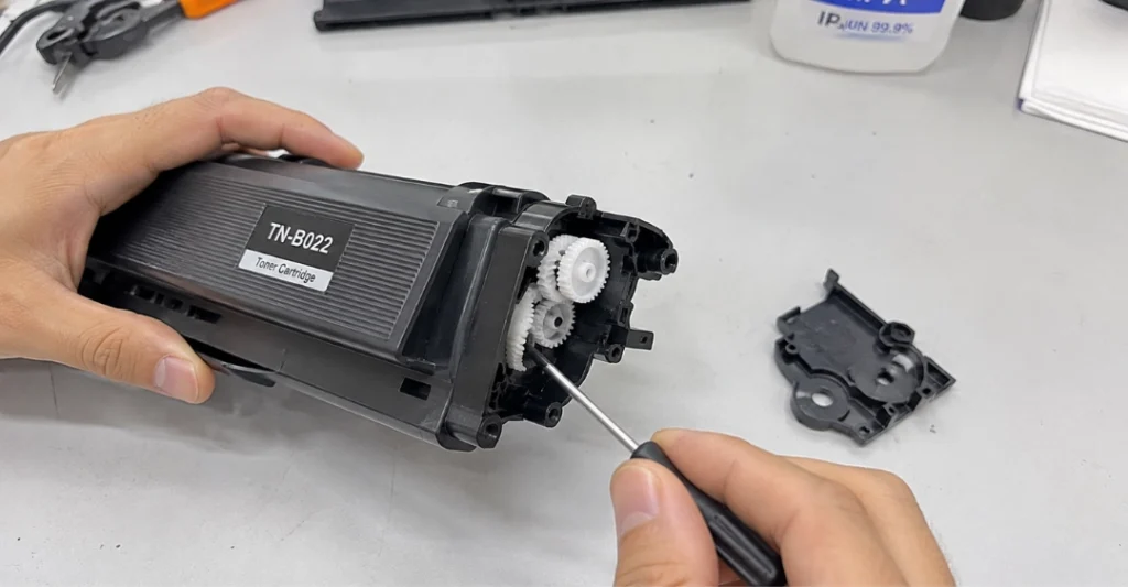 Tháo ốp nhựa và điều chỉnh bánh răng reset trên hộp mực Brother TN-B022